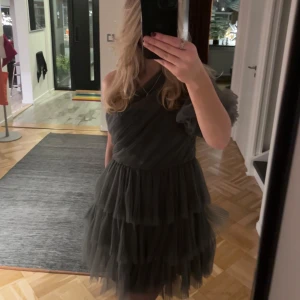 Grå By Malina Klänning Constance - Supersnygg grå kortklänning från Malina med flera lager volanger och en unik oneshoulder-design. Använd bara en gång och köptes för 3500kr. Hör av er så kan pris diskuteras. Storlek M men passar även mig som har S.