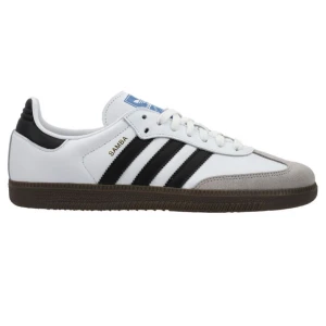 Adidas Samba vita sneakers - Klassiska Adidas Samba sneakers i vitt skinn med svarta ränder och detaljer, grå mocka framtill och brun gummisula. Ikonisk blå Adidas-logga på plösen och snörning framtill. Perfekta för en sportig och stilren look.