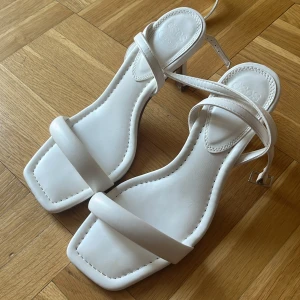 Vita sandaler med klack från ASOS - Stilrena vita sandaler från ASOS med fyrkantig tå, smala remmar och elegant klack. Skorna har en minimalistisk design och är tillverkade i syntetmaterial. Perfekta för dig som gillar en clean och modern look. Klackhöjd ca 8cm. Endast använda en gång 