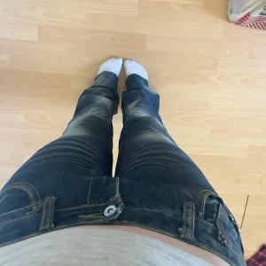 Mörkblå bootcut jeans med slitningar - Säljer ett par mörkblå jeans med snygga slitningar och ljusa partier på låren och knäna. Modellen är bootcut med låg midja och klassiska fickor bak, samt coola detaljer vid linningen. Perfekta för en avslappnad och trendig look. Köpta i spanien!