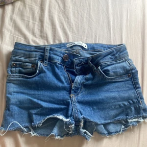 Blå jeansshorts från Zara - Snygga blå jeansshorts från Zara i storlek 32. Klassisk femficksmodell med rå, fransig kant nertill och dragkedja framtill. Perfekta för varma dagar och ger en avslappnad vibe. Tillverkade i denim med normal passform. Skriv för bilder på! 