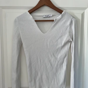 Vit ribbad långärmad tröja NA-KD - Säljer en vit ribbad långärmad tröja från NA-KD i storlek S. Tröjan har v-ringning och är figurnära med stretchigt material, perfekt att styla med jeans eller kjol. Enkel och clean look som funkar året runt.