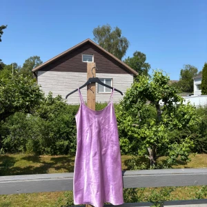 Lila satin kortklänning med snörning - Superfin lila kortklänning i glansigt satinmaterial med tunna axelband och snygg snörningsdetalj i ryggen. Inget lapp med varumärke eller storlek men passar mig som är S, även en storlek mindre eller större 