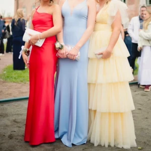 Röd långklänning med oneshoulder - Säljer en röd långklänning med oneshoulder och öppen rygg. Klänningen har smal passform, tunna axelband och knyt i ryggen. Snygg, minimalistisk design i ett glansigt material som ger en lyxig känsla. Perfekt för bal eller festkvällar.