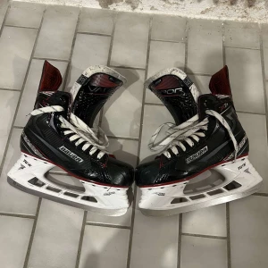 Bauer Vapor X700 hockeyskridskor 40,5 - Säljer ett par Bauer Vapor X700 hockeyskridskor i svart med röda och vita detaljer. Skridskorna har snörning och robust konstruktion i syntetmaterial, perfekt för dig som vill ha grym kontroll på isen.