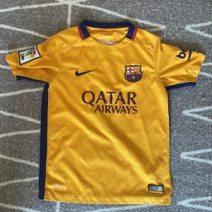 FC Barcelona Neymar 11 bortatröja Nike Barn M - Gul FC Barcelona bortatröja med Neymar JR 11 på ryggen. Tröjan har röda vertikala ränder bak, blå detaljer vid krage och ärmslut samt klubbmärke och Nike-logga fram. Tillverkad i Dri-FIT-material som andas. Sponsorer: Qatar Airways och UNICEF.