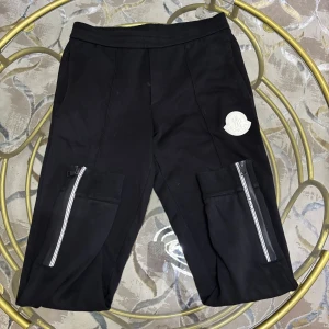 Svarta cargopants från Moncler - Svarta cargopants från Moncler med stora fickor på benen och coola dragkedjor med logga. Byxorna har en relaxed fit och är tillverkade i mjuk bomull. Stort Moncler-märke på ena benet ger en exklusiv vibe.