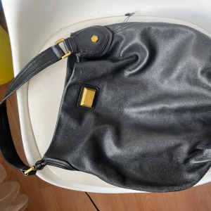 Svart axelväska i skinn med mönstrat foder - Cool svart axelväska i skinn med guldfärgade metalldetaljer och justerbart axelband. Insidan har ett rött och svart stjärnmönstrat foder samt innerfack med dragkedja. Perfekt för dig som vill ha en väska med lite edge och plats för allt du behöver 💕