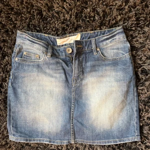 Blå jeanskjol från H&M - Snygg blå jeanskjol från H&M med klassisk femficksdesign, bälteshällor och dragkedja framtill. Kjolen har en lätt tvättad look och är perfekt för en avslappnad stil. Passar till allt och är enkel att matcha med olika toppar.