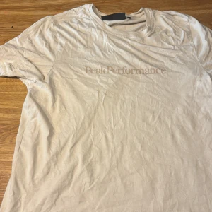 Beige Peak Performance t-shirt M - Snygg beige t-shirt från Peak Performance i mjuk bomull. Klassisk rund halsringning och diskret logga framtill. Perfekt basic-plagg med normal passform och korta ärmar. Enkel att matcha med jeans eller shorts.