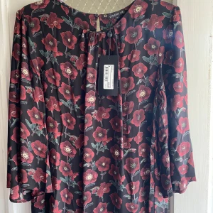 Blommig blus från STOCKH LM - Supersnygg blus med röda blommor från STOCKH LM. Långärmad modell med rund hals och knapp i nacken. Flowigt tyg som ger en avslappnad vibe. Perfekt för dig som gillar att sticka ut med ett blommigt mönster.