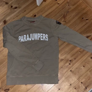 Beige sweatshirt från Parajumpers - Säljer en beige sweatshirt från Parajumpers med stor vit logga över bröstet och patch på ena ärmen. Tröjan har rund halsringning, långa ärmar och ribbade muddar. Perfekt för en chill och stilren look. Kan stylas grish och många andra sätt