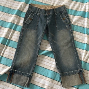 Blå croppade jeans från MNG Jeans - Snygga blå croppade jeans från MNG Jeans med stora fickor fram och bak, uppvikta benslut och coola slitningar. Jeansen har normal passform och är tillverkade i klassiskt denimtyg med orangea sömmar. Perfekta för en avslappnad streetstil.