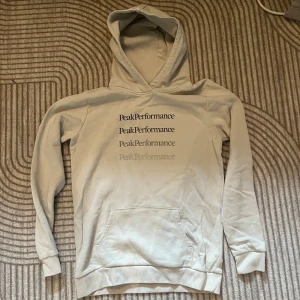 Beige hoodie från Peak Performance - Snygg beige hoodie från Peak Performance med tryck. Den är väldigt snygg och stilren. Det finns ett litet håll vid axel men som inte är något större. Hör gärna av er vid fler bilder
