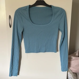 Ljusblå ribbad långärmad topp - Ljusblå ribbad långärmad topp med croppad passform och rundad, djup urringning. Tunt och stretchigt material som sitter snyggt på kroppen. Ena sömmen vid handen har gått upp men ser fortfarande fin ut:) Köparen står för frakt