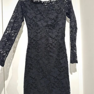 Svart spetsklänning från NLY Trend - Supersnygg svart klänning från NLY Trend i spets med lång ärm och figurnära passform. Klänningen har ett vackert spetsmönster över hela och är perfekt för dig som vill sticka ut. Fodrad underklänning och transparenta ärmar.