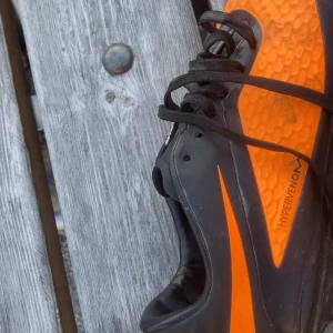 Nike Hypervenom fotbollsskor svart/orange - Nike Hypervenom fotbollsskor i svart och orange med coolt mönstrad ovandel och klassisk Swoosh. Skorna har snörning och en låg profil, perfekt för dig som vill sticka ut på planen. Snygg detalj med dödskalle på hälen. Kommer ej med box