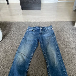 Blå jeans från Replay - Säljer ett par klassiska blå jeans från Replay med snyggt slitna detaljer och raka ben. Jeansen har fem fickor, normal passform och är tillverkade i robust denim. Perfekta för dig som gillar en tidlös och avslappnad stil.