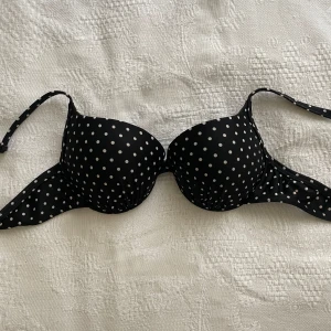 Svart bikiniöverdel med vita prickar - Snygg svart bikiniöverdel med vita prickar och vadderade kupor. Justerbara axelband och klassisk knäppning bak. Perfekt för dig som vill ha en retrovibe på stranden. Materialet känns mjukt och bikinis har använts få gånger. Oklart vilket märke då jag köpte den utomlands💕