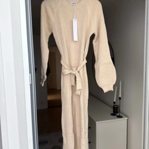 Beige stickad långklänning med knyt - Superfin beige stickad långklänning från BUBBLEROOM med ribbad struktur och ballongärmar. Klänningen har ett brett knytband i midjan som ger en snygg siluett. Nyrpis 599:-. Prislapp kvar. 
