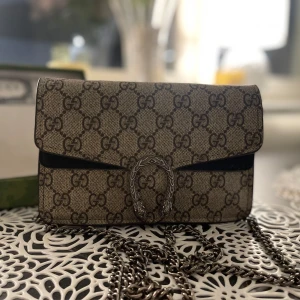 Gucci Dionysus axelväska med GG-mönster - Säljer en Gucci Dionysus axelväska i beige och brunt GG Supreme-mönster. Väskan har en snygg silverfärgad kedja och ikoniskt spänne med ormdetaljer. Tillverkad i canvas med skinn-detaljer. Perfekt för dig som vill ha en statementväska från Gucci.
