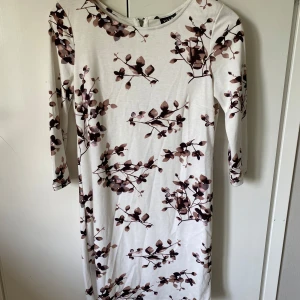 Blommig klänning från Vila - Säljer en vit klänning från Vila med brunt blommigt mönster. Klänningen har trekvartsärm och dragkedja i ryggen. Perfekt för vår och sommar, i mjukt och bekvämt material. Storlek XS men funkar till S och mindre Medium också.