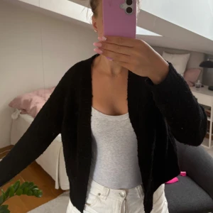 Svart stickad kofta från AWARE XS - Svart stickad kofta från AWARE i storlek XS. Koftan har en enkel, öppen design utan knappar och är långärmad. Perfekt att slänga över ett linne eller t-shirt för en chill och stilren look. Använd men i bra skick