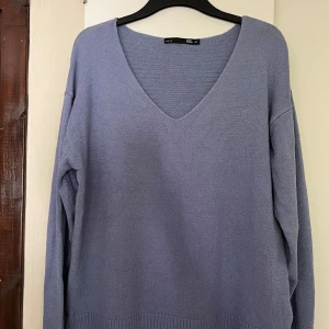 Ljuslila stickad tröja från 157 - Mysig ljuslila stickad tröja från 157 med djup v-ringning och lång ärm. Tröjan har en relaxed passform och ribbade muddar vid ärmslut och nederkant. Perfekt att slänga på sig när du vill vara både chill och snygg.