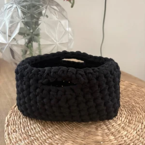 Svart handvirkad handväska - Unik svart handväska som är grovt virkad för en chunky look. Väskan har ett ovalt format och praktiska handtag som är integrerade i designen. Perfekt för dig som gillar handgjorda accessoarer med personlig touch.