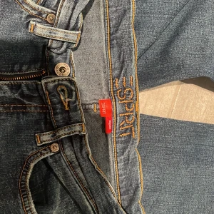 Blå bootcut jeans från Esprit - Snygga blå jeans från Esprit med bootcut passform och broderade bakfickor. Jeansen har klassisk femficksdesign, orange kontrastsömmar och dragkedja. Passar som storlek 34-38 ungefär, kontakta för exakta mått! Dom är vintage och säljs inte längre.