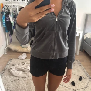 Grå velour hoodie från Gina Tricot - Mysig grå hoodie i velour från Gina Tricot med dragkedja framtill och huva. Jackan har två fickor fram och ribbade muddar vid ärmslut och nederkant. Perfekt för chill dagar eller när du vill ha en soft look.