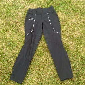 Svarta ridleggings från Copperfield - Svarta ridleggings från Copperfield med hög midja och snygga silikongrepp på insidan av benen och sätet. Tillverkade i stretchigt material med 75% polyamid och 25% spandex. Snygga vita detaljer och logga framtill. Perfekta för ridning och riktigt bekväma.