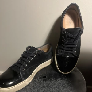 Mörkblåa lanvins - Snygga svarta sneakers från Lanvin med ovandel i mocka och lackad tå. Skorna har vita gummisulor och klassisk snörning. Perfekta för dig som gillar stilrena och exklusiva sneakers med en lyxig touch. Priset kan diskuteras 