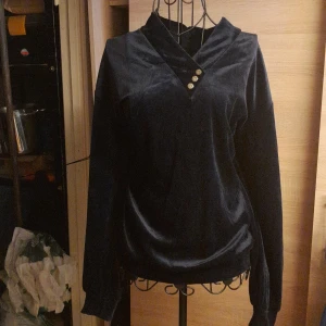 Mörkblå sammetströja med knappar - Mysig mörkblå tröja i sammet med lång ärm och snygg v-ringning framtill. Tre dekorativa knappar vid halsen ger en extra touch. Perfekt för dig som gillar en lite lyxigare känsla i vardagen.