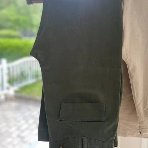 Olivgröna byxor - Snygga olivgröna byxor med fickor både fram och bak (ej riktiga bak). Byxorna har hög midja, bälteshällor och stängs med knapp och dragkedja. Materialet är svalt och lätt samtidigt som det är väldigt fint på utsidan. (Oanvända. Står också strl 42 på insidan men det är mindre)