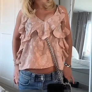 Ljusrosa ZARA volanglinne med spetsdetaljer - Säljer ett ljusrosa linnetopp från zara med tunna axelband och volangdetaljer framtill och längs sidorna. Toppen har ett subtilt blommönster och är perfekt för varma dagar. Supersöt och feminin stil!