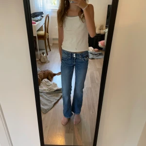 Blå bootcut jeans med låg midja - Säljer ett par klassiska blå jeans med bootcut och låg midja. Jeansen har snygga slitningar framtill, dubbla knappar och fem fickor. Perfekta för dig som gillar en avslappnad och tidlös look. Materialet är mjukt denim som sitter skönt hela dagen. Pris går att diskuteras 