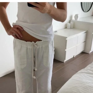 Roxy linnebyxor med prislapp kvar - Säljer ett par vita linnebyxor med breda ben och dragsko i midjan. Byxorna har två stora fickor framtill och är tillverkade i svalt linnematerial, perfekta för varma dagar. De har en avslappnad passform och midjan kan justeras med snöret.