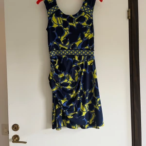 Blågul blommig kortklänning - Snygg kortklänning från Lauren Ralph Lauren med blått och gult blommönster. Klänningen har breda axelband, markerad midja med grafiskt band och lätt drapering i sidan. Perfekt för dig som gillar färg och mönster! Inte säker på att det är Ralph Lauren men köpt i design affär i St Topez. 