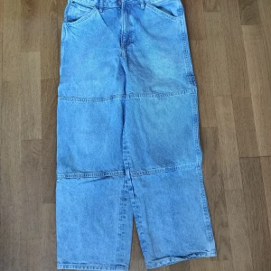Baggy ljusblå cargopants i jeans - Säljer ett par riktigt schyssta ljusblå cargopants i jeansmaterial. Byxorna har bred passform, stora fickor på sidorna och coola sömdetaljer över benen. Perfekta för dig som gillar avslappnad streetstil och vill sticka ut lite extra.