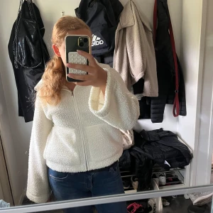 Vit mysig teddyjacka från Lager157 - Mysig vit teddyjacka med dragkedja framtill och stora fickor. Jackan har en bred krage och är tillverkad i fluffigt fleece-material som ger en chill och trendig look. Perfekt för mysiga kvällar.
