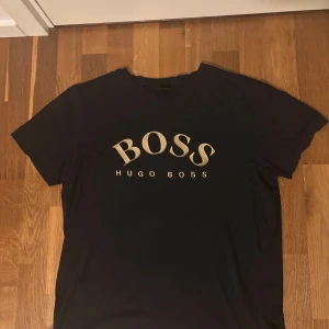 Svart t-shirt från Hugo Boss - Svart t-shirt från Hugo Boss med stort guldigt BOSS-tryck på bröstet. Storlek XL men sitter som L