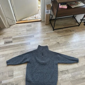 Grå stickad tröja med half zip - Mysig grå stickad tröja med hög krage och half zip-dragkedja. Perfekt för kyliga dagar och enkel att matcha med jeans eller leggings. Tröjan har långärmad passform och en lite loose siluett för extra komfort.