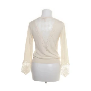 Beige topp med spetsdetaljer - Superfin beige topp med långärmade spetsdetaljer vid ärmsluten och en djup v-ringad rygg i spets. Tunt och mjukt material som ger en romantisk vibe. Perfekt för dig som gillar feminina och unika plagg.