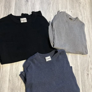 3-pack basic tröjor från Cope - Säljer tre stilrena basic tröjor från Cope i svart, grått och mörkblått. Alla har rund halsringning, lång ärm och ribbade muddar. Perfekta att matcha med jeans eller chinos för en clean look. Materialet känns mjukt och lätt, troligen bomull eller bomullsblandning.