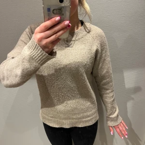 Beige stickad tröja - Säljer en mysig beige stickad tröja med rund hals och långa ärmar. Perfekt för kyliga dagar och enkel att matcha med olika outfits. Tröjan har en mjuk och bekväm passform.