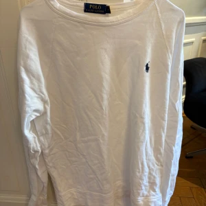 Vit långärmad tröja från Polo Ralph Lauren - Säljer en klassisk vit långärmad tröja från Polo Ralph Lauren. Tröjan har en liten broderad logotyp i marinblått på bröstet och är tillverkad i mjuk bomull. Perfekt för en stilren och avslappnad look.