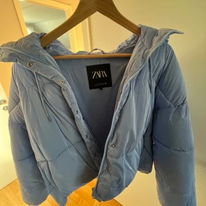 Ljusblå pufferjacka från Zara - Säljer en snygg ljusblå pufferjacka från Zara. Jackan har en dragkedja framtill och en mysig huva.