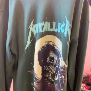 Grön långärmad Metallica-tröja - Säljer en grön långärmad tröja med Metallica-tryck. Tröjan har ett stort motiv på framsidan och texten 'I'm inside, open your eyes' längs ärmen. Perfekt för fans av bandet!