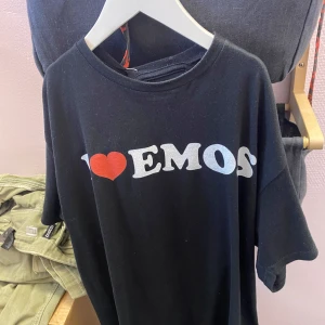 Svart t-shirt med tryck - Cool svart t-shirt med texten 'I ❤️ EMOS' i vitt och rött. Perfekt för dig som vill uttrycka din stil med ett statement. T-shirten har en klassisk passform och korta ärmar.